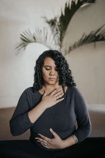 reiki practitioner with one hand on her heart and one hand on her belly and her eyes closed
