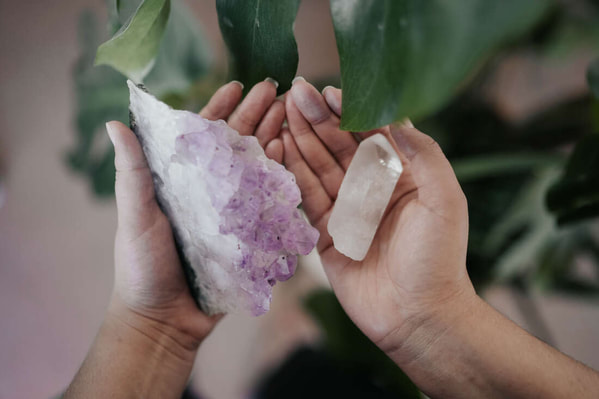 holistic coach's hands holding one amethyst crystal and one quartz crystal